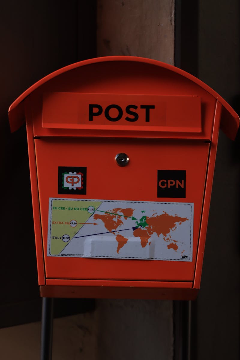 Close-up of a bright orange mailbox labeled 'POST' with a world map design and logos.